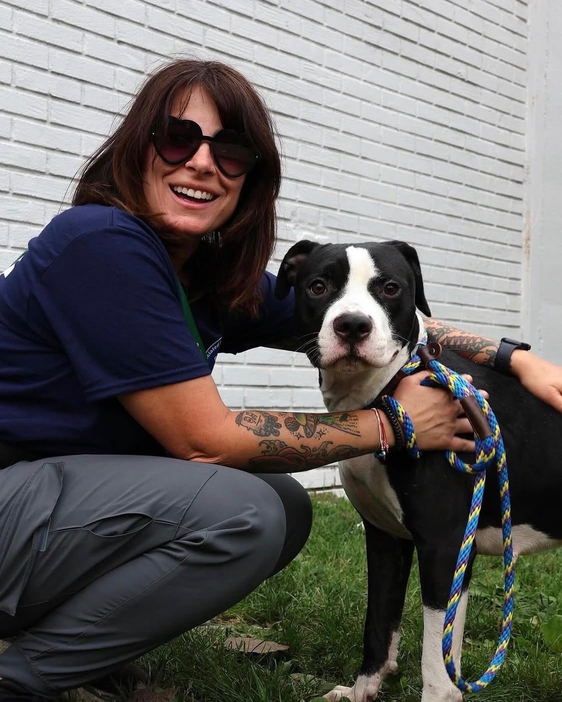 Erica Piancone crouched beside a black-and-white pit bull on a leash, both looking at the camera